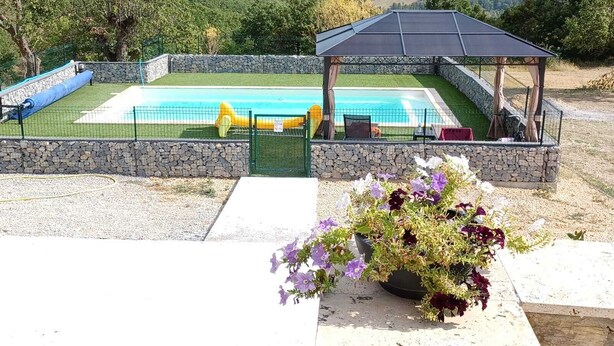 Une piscine avec une terrasse en pierre, un espace salon couvert et une composition florale.