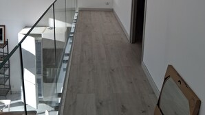Un hall d’entrée spacieux, doté d’un plancher en bois, d’une rambarde en verre sur le côté gauche et d’une porte sur le côté droit.