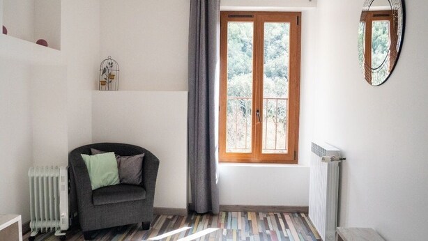 Ein Zimmer mit Fenster, Heizkörper, Stuhl und Spiegel an der Wand.