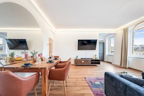 Ein modernes Wohnzimmer mit einem Holzesstisch, Ledersesseln, einem Flachbildfernseher und großen Fenstern.