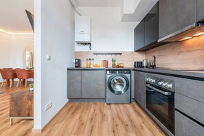 A compact kitchen with a washing machine, oven, and a dining area with chairs. - Artistic Apartment, 1-Bedroom, Flat TV (Vienna)