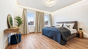 Ein modernes Schlafzimmer mit einem großen Bett, einem Nachttisch, einer Pflanze und Blick ins Freie.