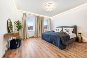 Ein modernes Schlafzimmer mit einem großen Bett, einem Nachttisch, einer Pflanze und Blick ins Freie.
