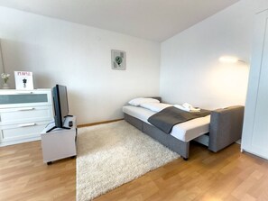 Ein modernes Schlafzimmer mit einem Bett, einem Nachttisch, einem Fernseher und einer weißen Kommode.