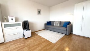 Ein Zimmer mit grauem Sofa, weißem Schminktisch und einem kleinen weißen Tisch mit Lampe.