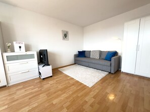 Ein Zimmer mit grauem Sofa, weißem Schminktisch und einem kleinen weißen Tisch mit Lampe.