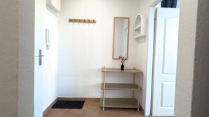Ein Flur mit einer weißen Tür, einem Spiegel, einem Holzregal und einer schwarzen Matte auf dem Boden.