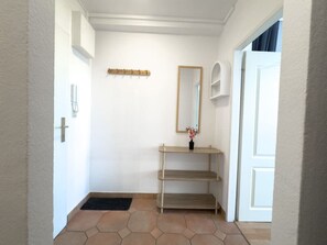 Ein Flur mit einer weißen Tür, einem Spiegel, einem Holzregal und einer schwarzen Matte auf dem Boden.