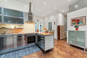 Une cuisine moderne dotée d’appareils électroménagers en acier inoxydable, d’un parquet en bois disposé en chevrons et d’un petit îlot central.