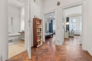 A spacious room with a wooden floor, a large bookshelf, a bed, and a bathroom with a bathtub and shower. - 2Bedroom Vintage Apartment+Garden, near Schönbrunn (Vienna)
