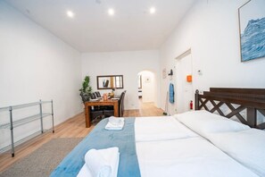 Ein Hotelzimmer mit einem Bett, einem Schreibtisch, einem Sessel, einem kleinen Tisch, einem Spiegel und einer Tür zu einem anderen Raum.