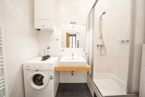 Ein kleines Badezimmer mit Waschmaschine, Waschbecken und Duschbereich.