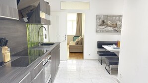 Een moderne keuken met een zwart aanrecht, roestvrijstalen apparatuur en uitzicht op een zithoek met een bank en een schilderij.