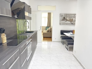 Eine moderne Küche mit schwarzem Arbeitsplatz, Edelstahlgeräten und Blick in einen Wohnbereich mit einer Couch und einem Gemälde.