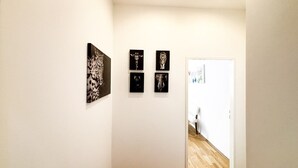 Een gang met vier ingelijste kunstwerken aan de muur, die leidt naar een kamer met een witte deur.