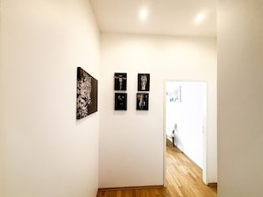Ein Flur mit vier gerahmten Kunstwerken an der Wand, der zu einem Raum mit einer weißen Tür führt.