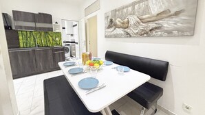 Een moderne keuken met donkere kastjes, een wit aanrecht en een eethoek met een witte tafel gedekt voor twee personen.