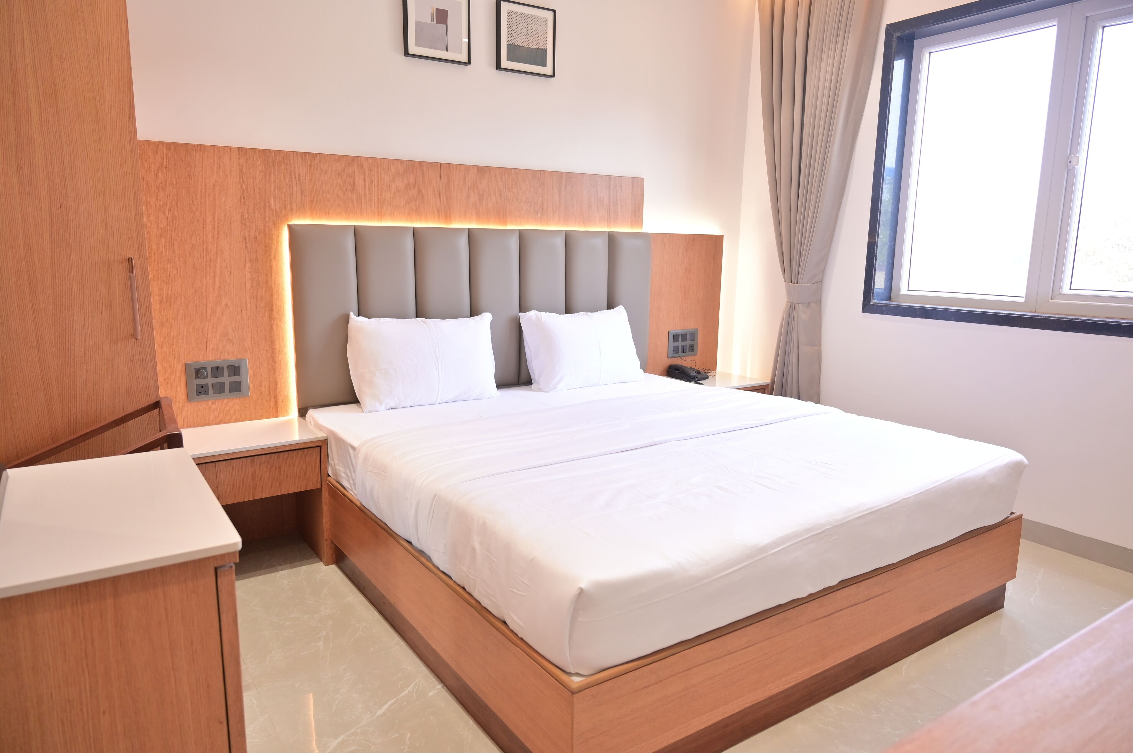 Una habitación de hotel moderna con una cama grande, cabecera de madera, mesitas de noche y una ventana con cortinas.