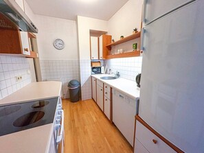 A compact kitchen with a stove, sink, and refrigerator, wooden cabinets, and a clock on the wall. - Studio mit Balkon, im Zentrum, Klimaanlage (Vienna)
