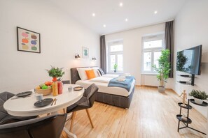 Ein modernes Hotelzimmer mit Bett, Essbereich, Fernseher und einem Fenster mit Vorhängen.