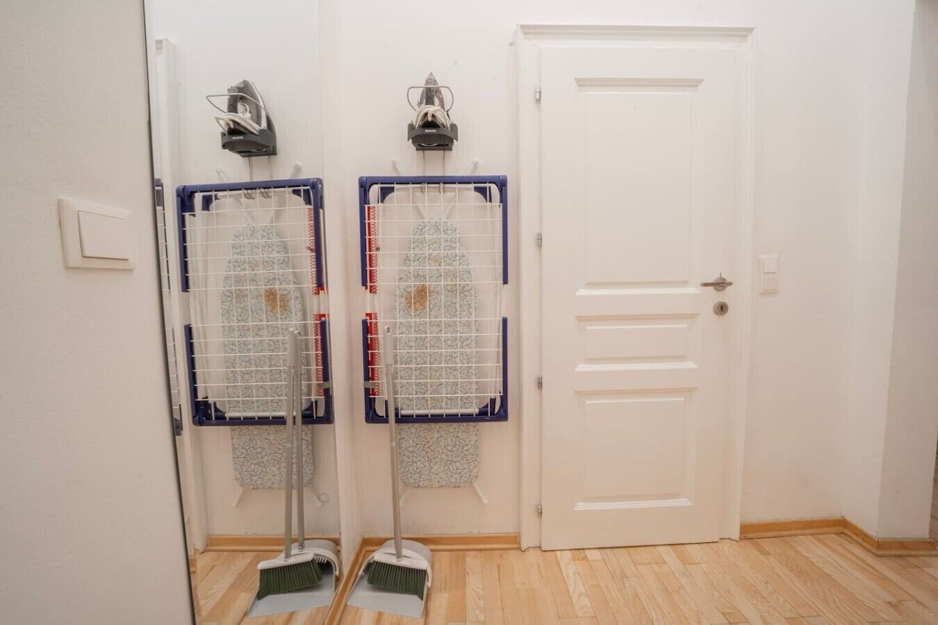 Une pièce avec une porte blanche, deux étendoirs fixés au mur et un balai appuyé contre le mur.