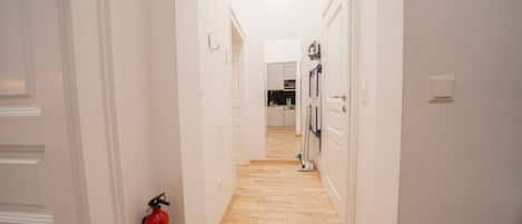A hallway with white doors, a fire extinguisher, and a kitchen area in the distance.