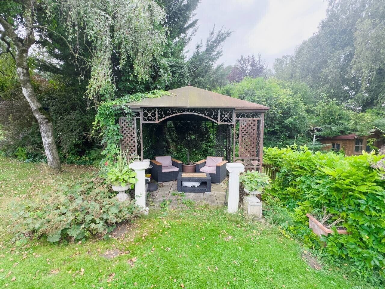 Un belvédère doté d’un toit en treillis et d’un espace salon, entouré d’une végétation luxuriante et d’arbres.