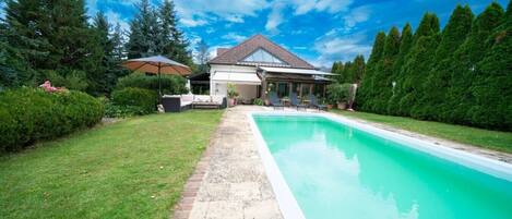 A house with a swimming pool, a covered patio, and a well-maintained lawn.