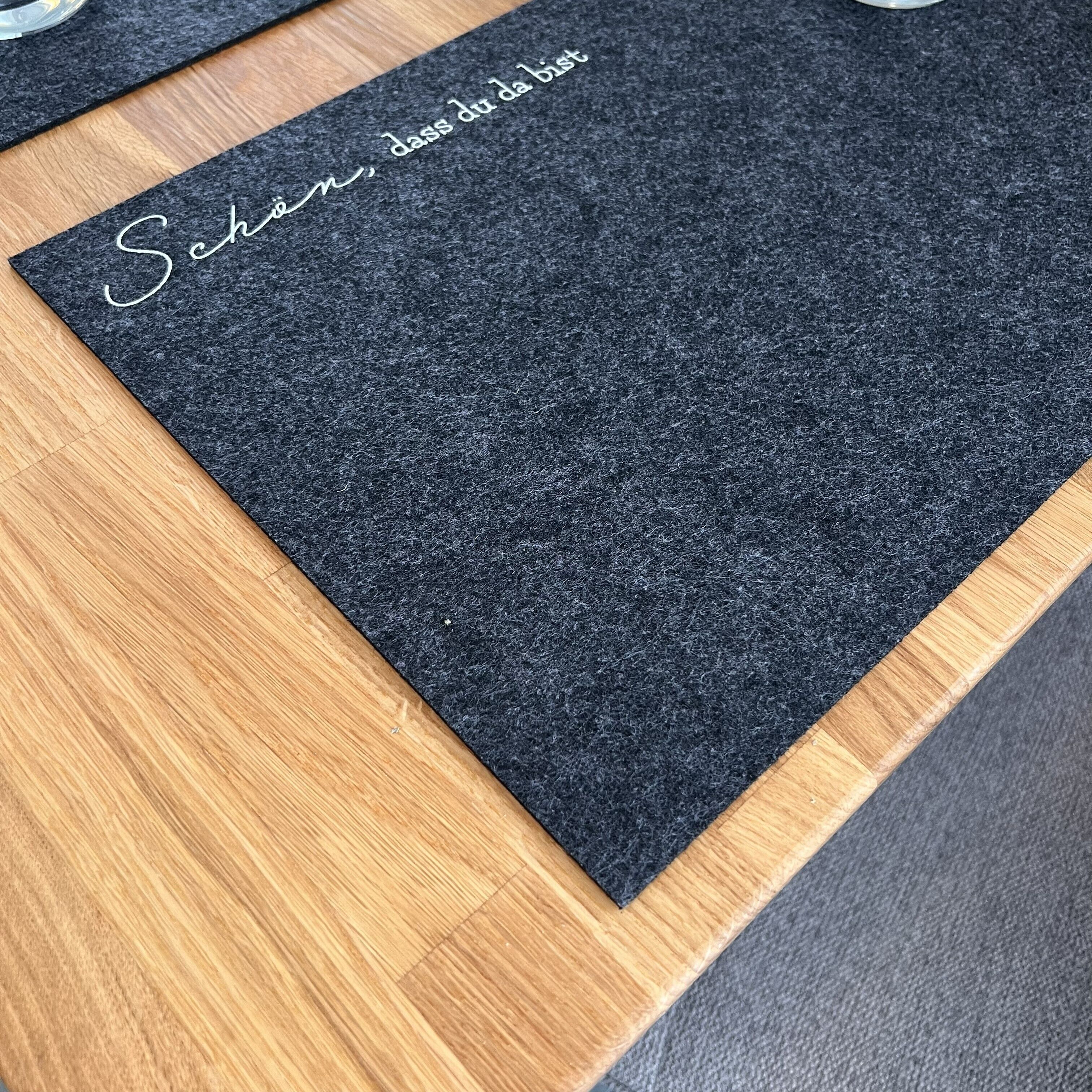 A black felt placemat with the text "Saison, dass du bist" on a wooden table.