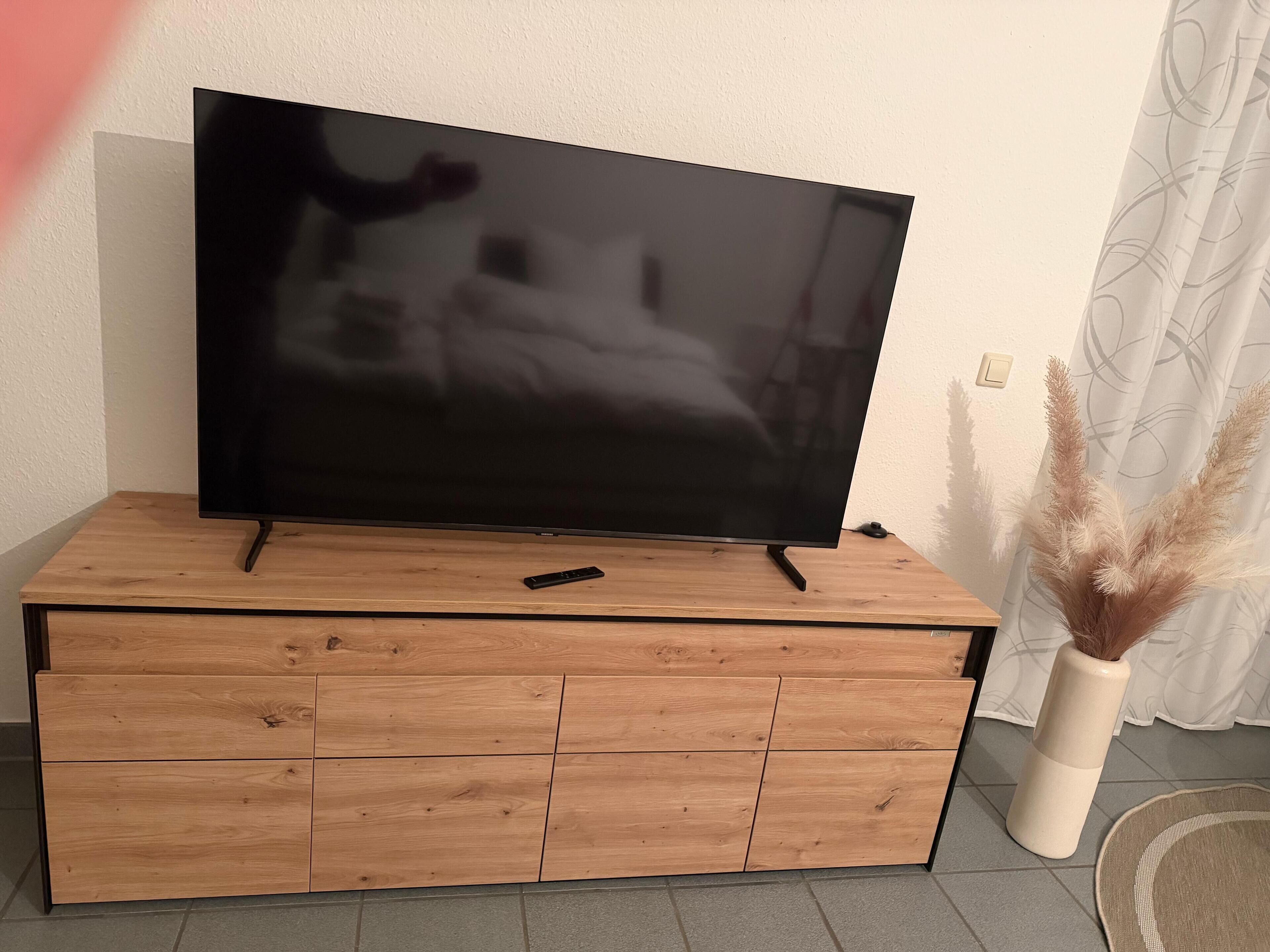 Ein Flachbildfernseher auf einer Holzeinrichtung, mit einer Fernbedienung darauf.