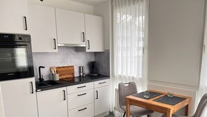 A modern kitchen with white cabinets, a black countertop, a built-in oven, and a dining area with a table and chairs. - Vacation apartment Allensbach (Allensbach)