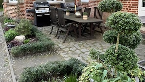 An outdoor patio with a barbecue grill, a table with chairs, and a large umbrella.