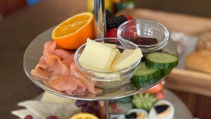 A multi-tiered food platter with various cheeses, meats, fruits, and vegetables.
