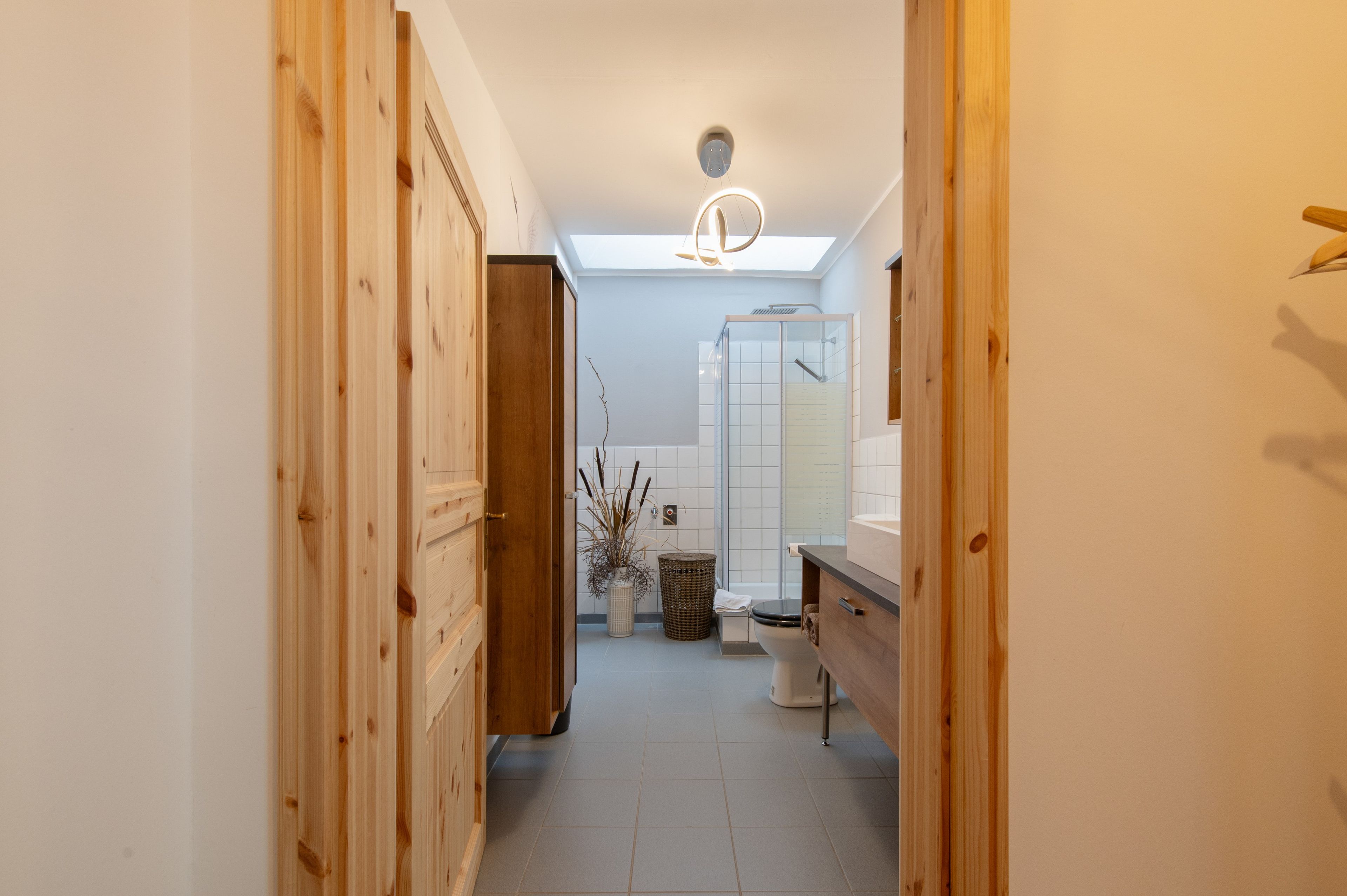 Ein schmaler Flur führt zu einem Badezimmer mit Dachfenster, Dusche und Toilette.