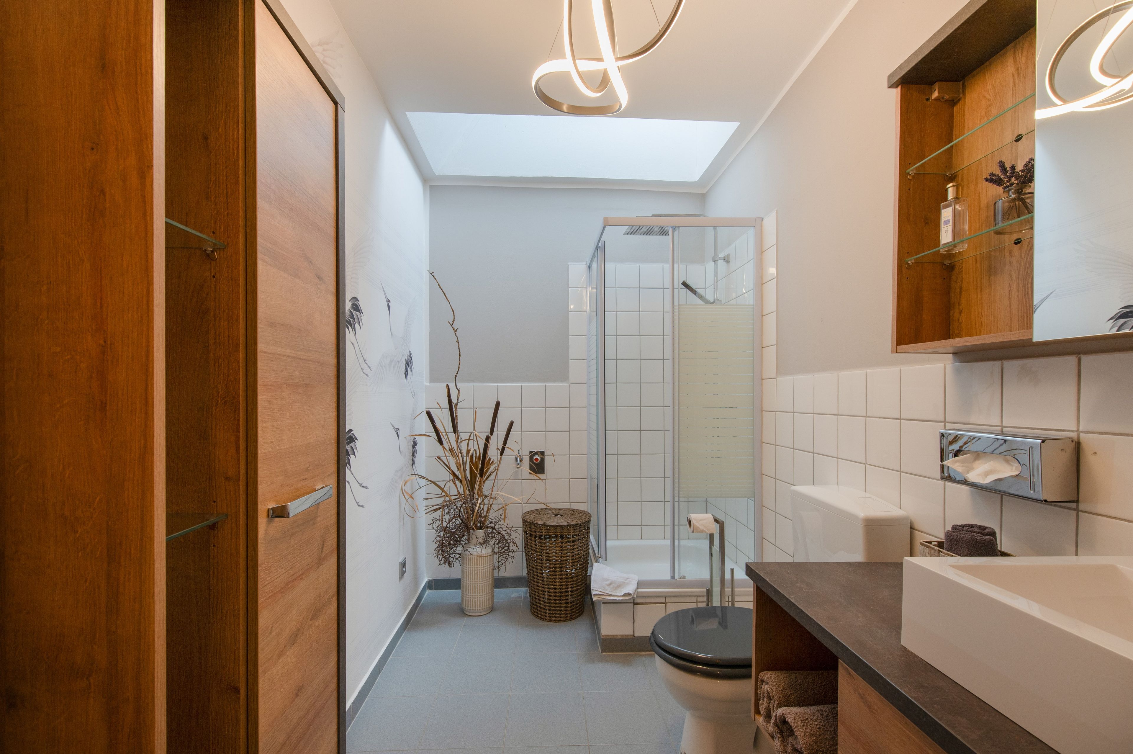 Ein modernes Badezimmer mit Dachfenster, einer Duschkabine aus Glas und Holzschränken.