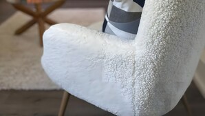 Ein weißer, strukturierter Sessel mit gestreiftem Kissen in einem modernen Wohnzimmer mit einem dunklen Sofa, einem Glastisch und einem Kamin.
