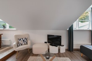 Ein modernes Wohnzimmer mit einer Couch, einem Sessel, einem Flachbildfernseher und einem kleinen Tisch.