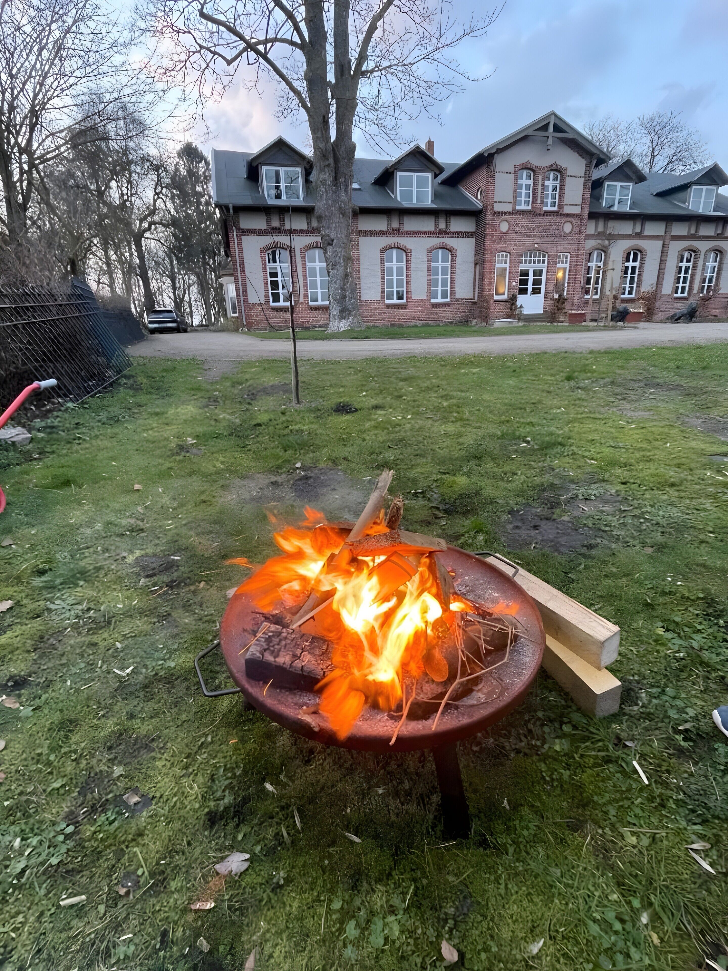 Nurmikolla on nuotiopaikka, ja taustalla näkyy tiilestä rakennettu rakennus.