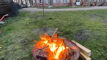 Nurmikolla on nuotiopaikka, ja taustalla näkyy tiilestä rakennettu rakennus.