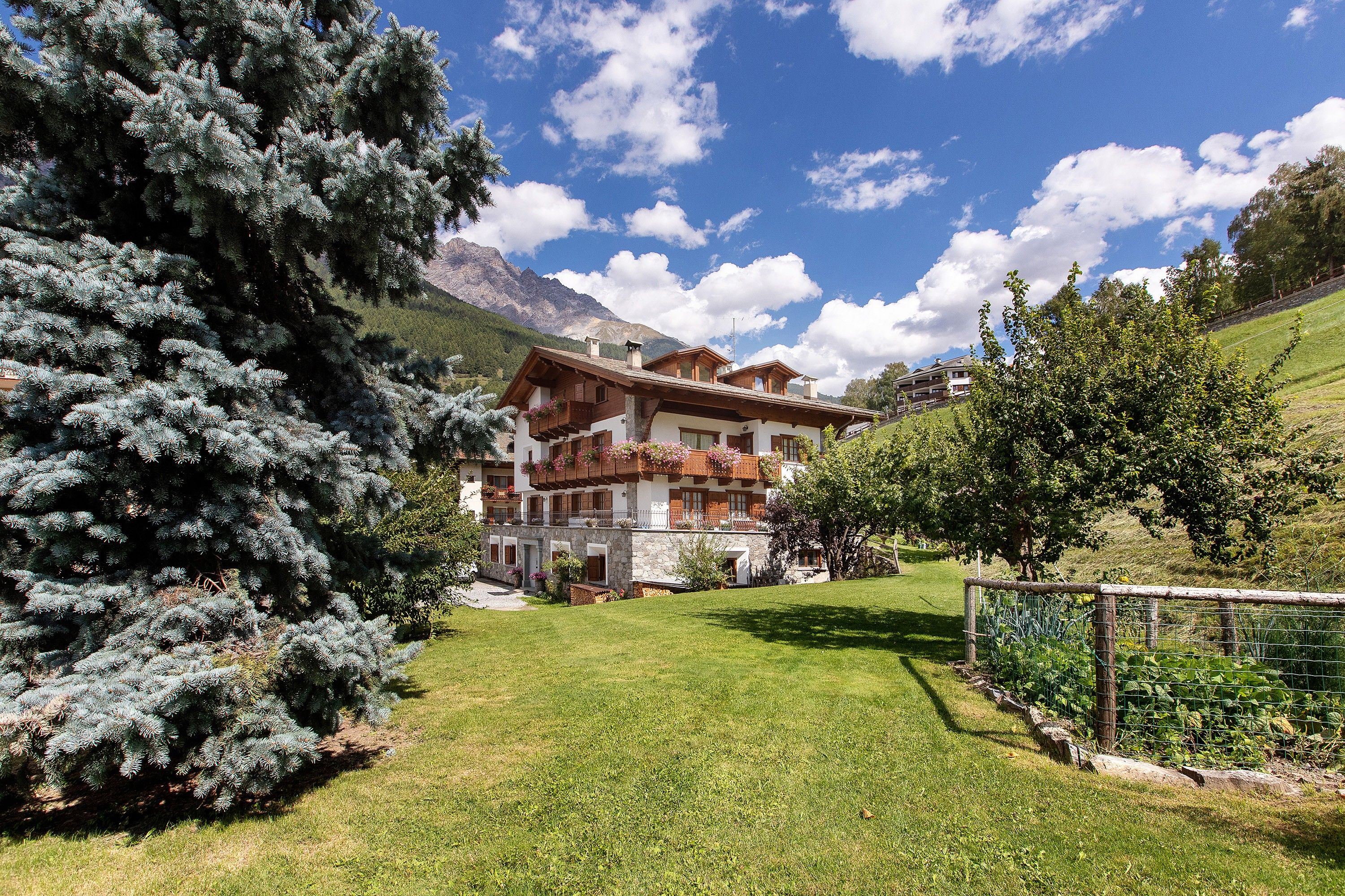 Un edificio in stile chalet con facciata in pietra, balconi in legno e vista su una catena montuosa.