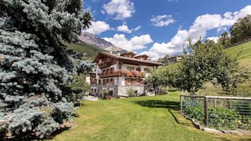 A chalet-style building with a stone facade, wooden balconies, and a view of a mountain range.