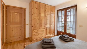 A room with a bed, wooden wardrobe, and a window with curtains. - Apartment 'Fior Di Montagna' with Mountain View, Shared Terrace and Wi-Fi (Bormio)