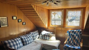 A cozy attic bedroom with a checkered sofa, a small table with a book and a remote, and a chair with a checkered cover. - Große Ferienwohnung 1 Oberzarten im Gästehaus Lickert (Hinterzarten)