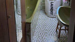 A compact bathroom with a green bathtub, a sink, and a skylight. A white laundry bag is visible. - Große Ferienwohnung 1 Oberzarten im Gästehaus Lickert (Hinterzarten)