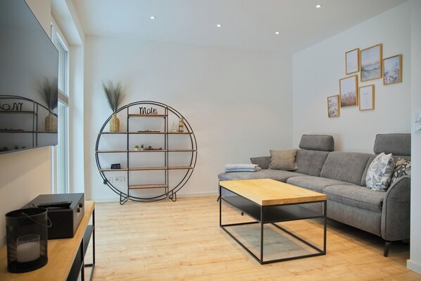 Un salon moderne avec un canapé gris, une table basse en bois et une étagère circulaire sur laquelle est inscrit le mot « Main ».
