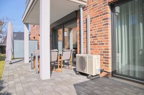 Un espace extérieur abrité, avec une table et des chaises, un mur en briques et une grande fenêtre.