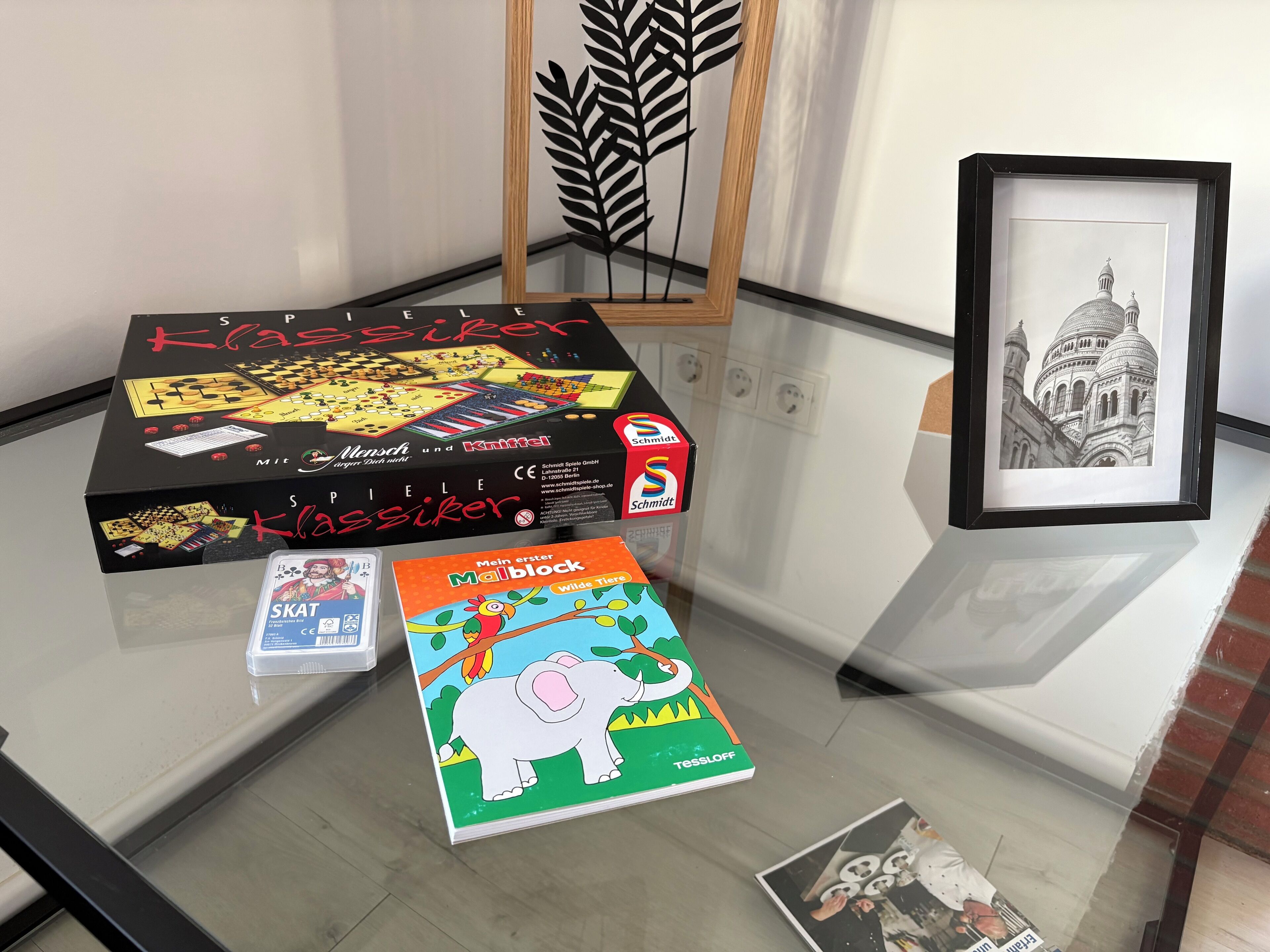 A glass table with a chess set, a book, and a framed picture.