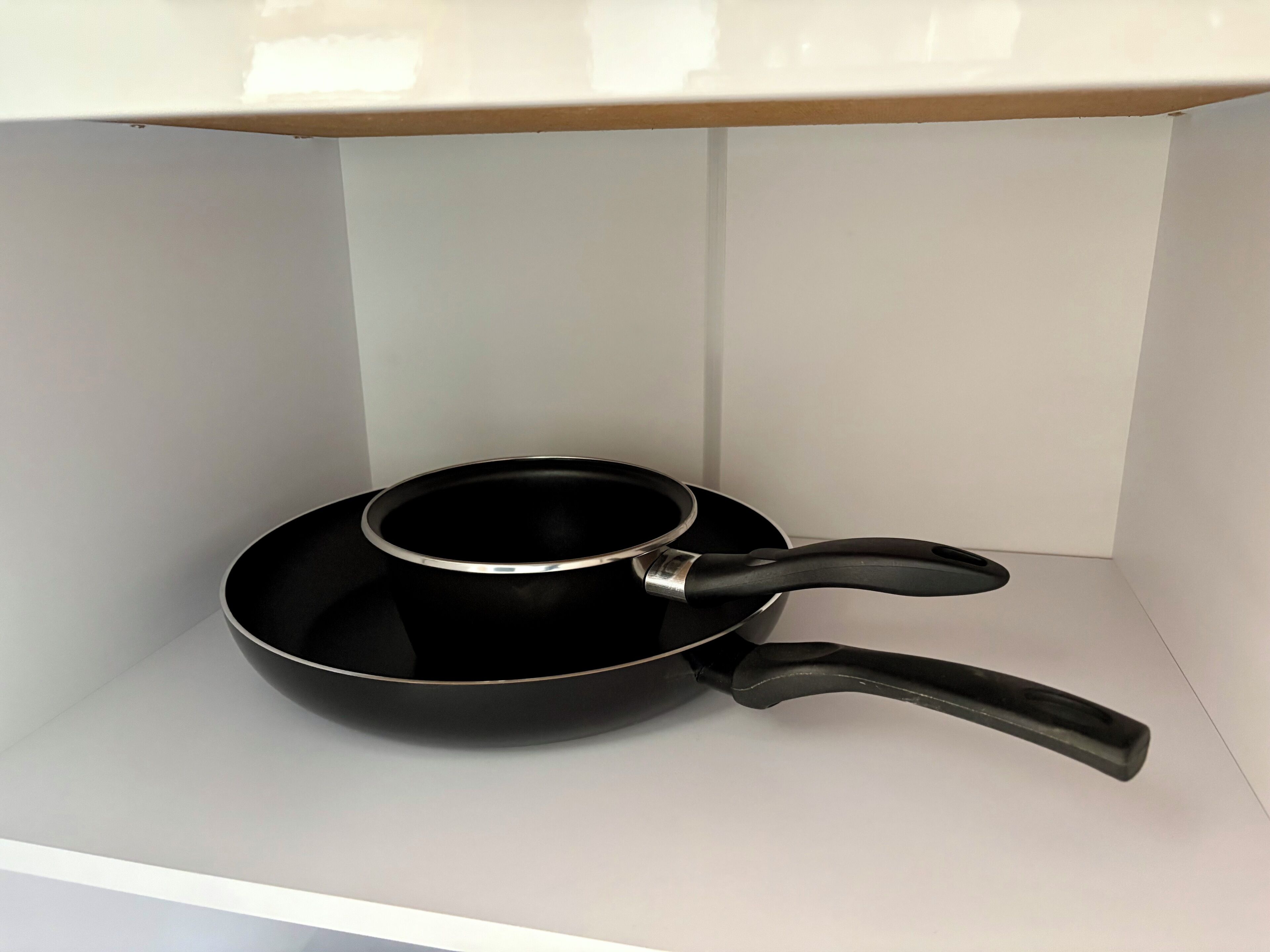 A black frying pan with a handle on a white shelf.