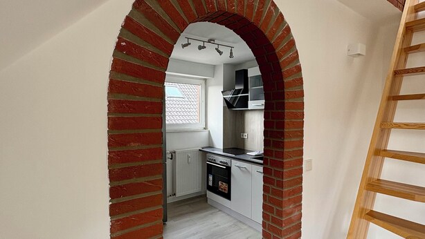 Una cocina con un arco de ladrillo, una ventana y una escalera de madera.