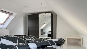 Un dormitorio moderno con una cama grande, tragaluces y vista a una habitación contigua.